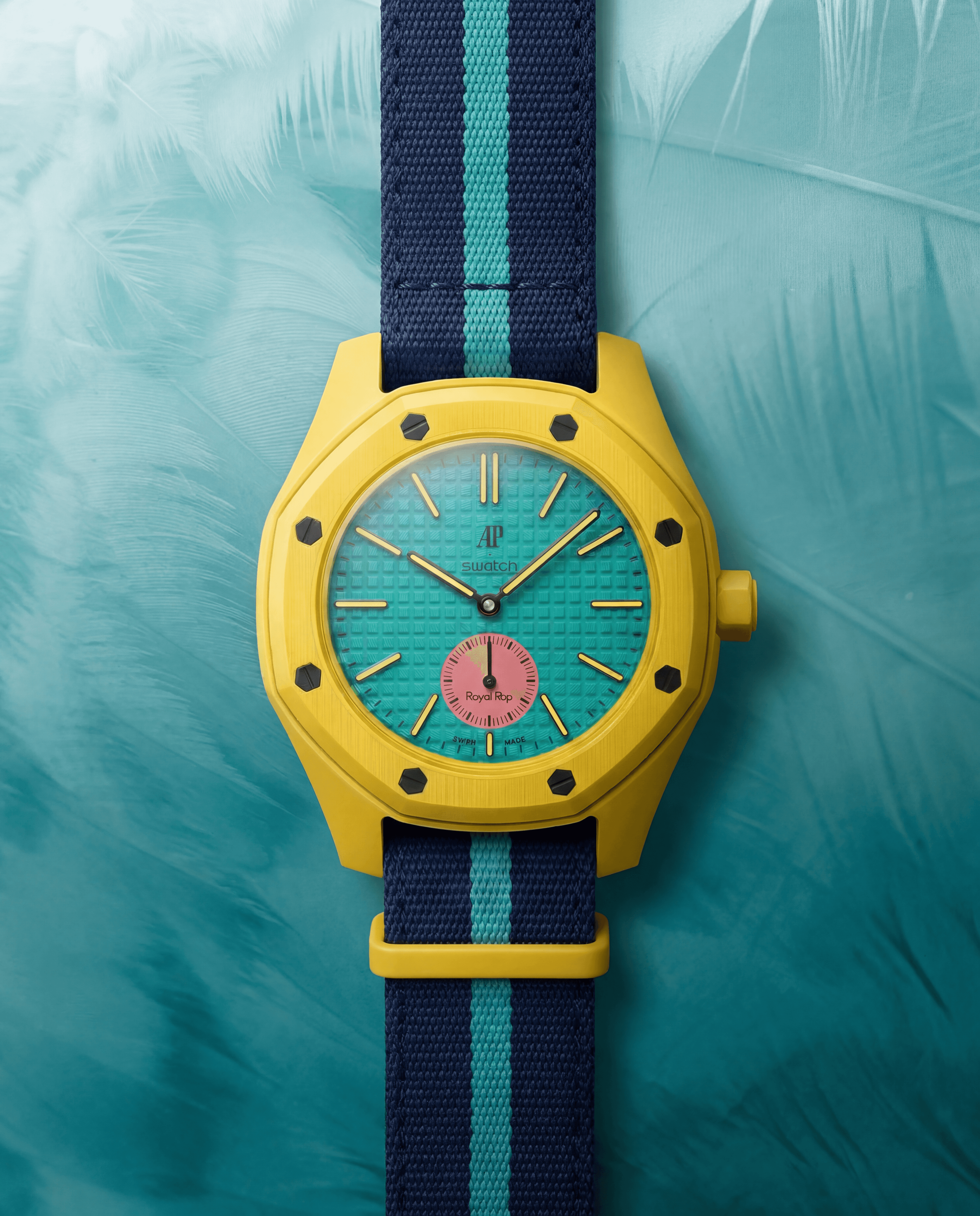 Mango Reef: yellow ceramic AP × Swatch Royal Pop with teal tapisserie dial and pink sub-dial, on a navy and teal striped NATO strap against a feathery teal backdrop.